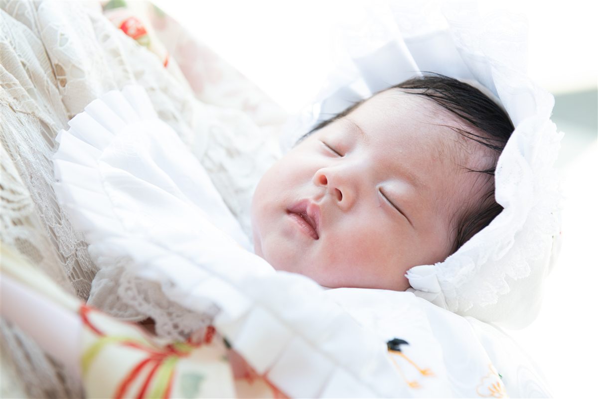 白い祝い着に包まれて眠るお宮参りの赤ちゃん