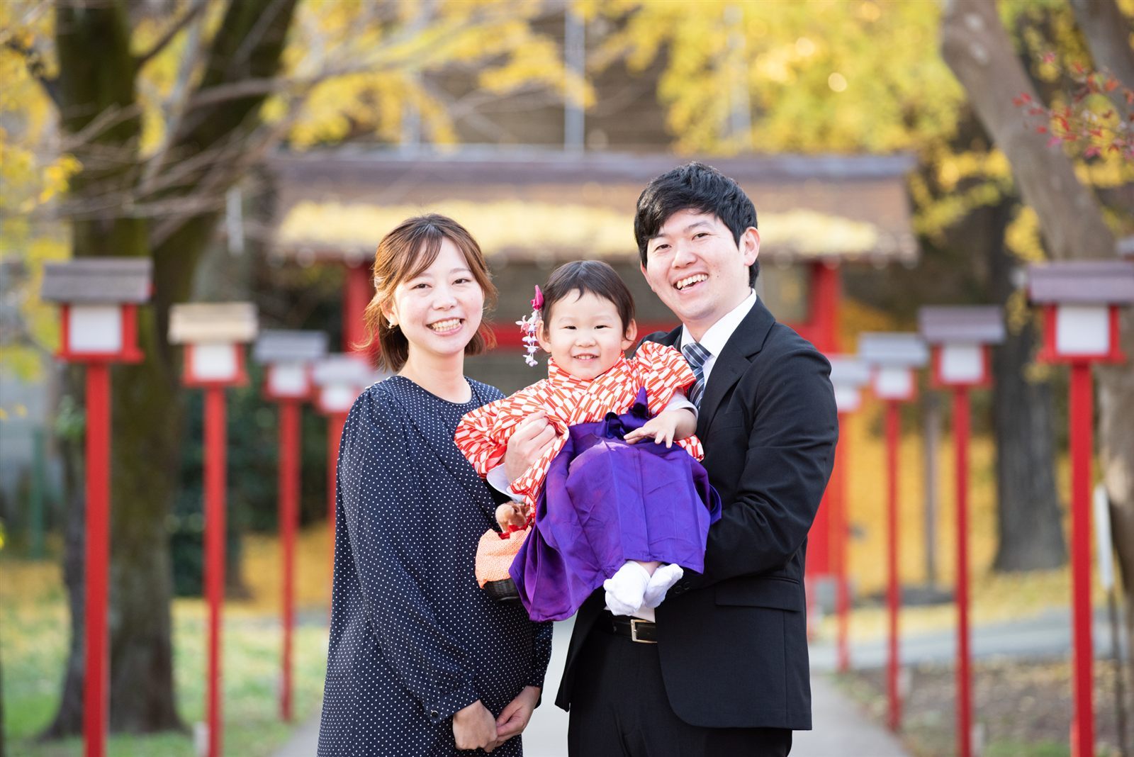 神社の参道で赤ちゃんを抱くお宮参りのご家族3人